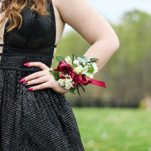 A woman's hand wearing a corsage on a black dress in an outdoor setting.