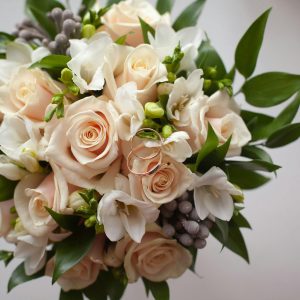 From above of composition of blooming flower bouquet with gentle rose petals and green spiky leaves on white floor